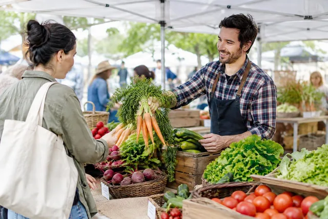 Farmers Market Seller Handing Carrots