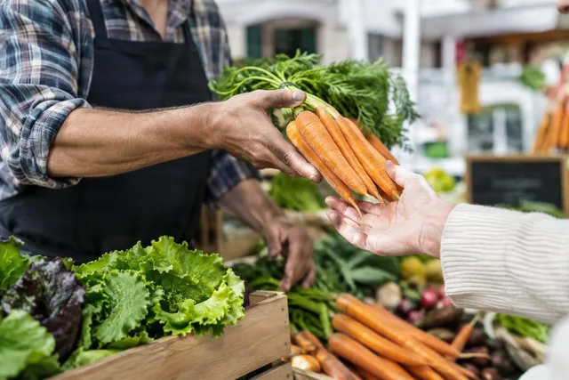 Vendor Handing Fresh Carrots