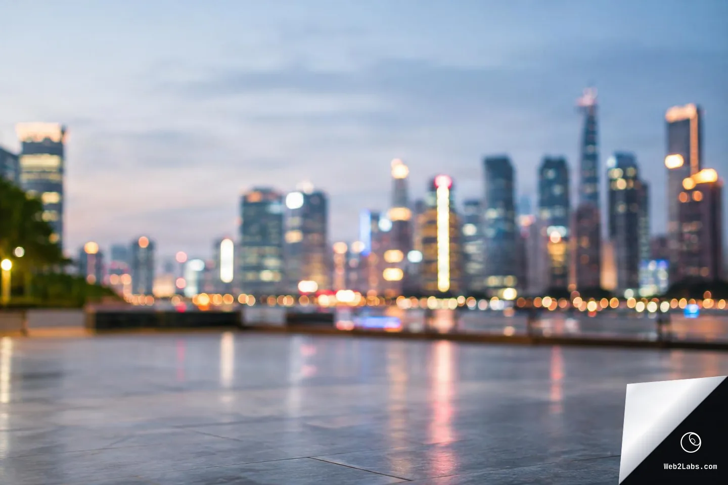 Soft-focus city skyline at dusk with bokeh lights across the horizon and an empty stone plaza in the foreground, with light reflections on the ground.