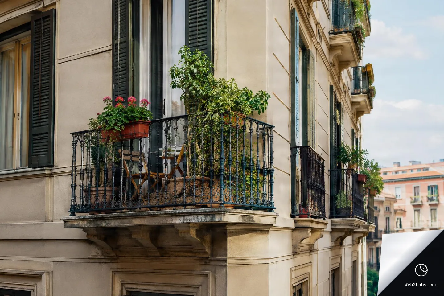 Corner view of a beige apartment building with a small wrought-iron balcony filled with potted plants and flowers, with additional balconies receding into the distance under a blue sky.