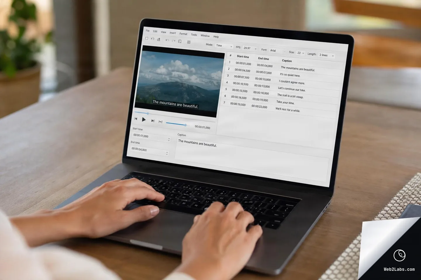 Hands typing on a laptop keyboard with a subtitle editing program open, showing a video preview of mountains and a table of caption lines with start and end times.